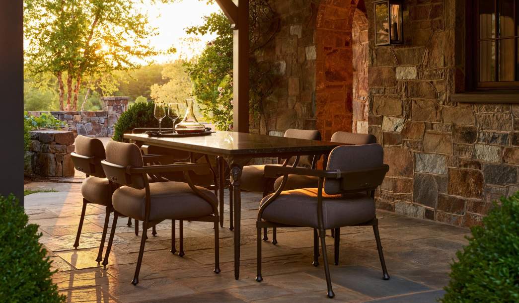 Dionysus Sculptura Dining Table and Bastille Dining Arm Chairs on a stone terrace at sunset