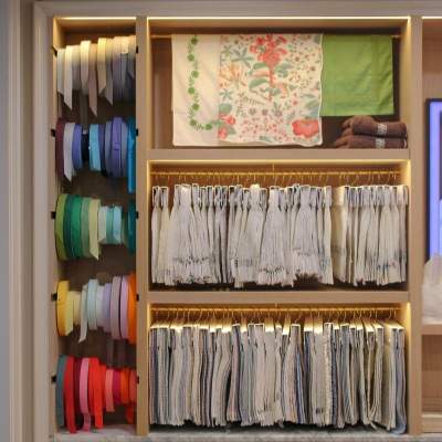 A built-in wooden display cabinet filled with neatly organized, colorful rolls of fabric, trims, and tassel passementerie.
