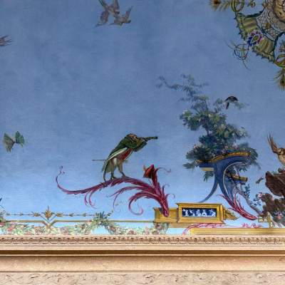 Detailed view of an ornate, sky-blue painted ceiling featuring delicate floral garlands, gilded scrollwork, and a bird in flight.