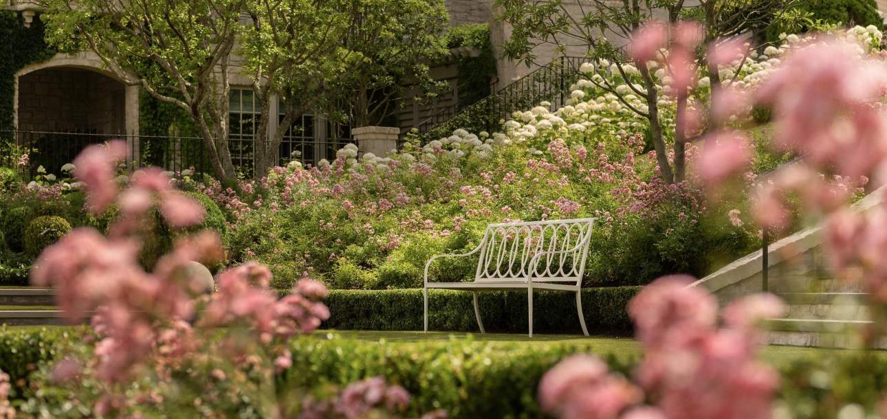 McKinnon and Harris Virginia Bench with Buie Back on a grassy lawn with flowers in bloom. Design by Beth Webb, Landscape Architect by Stephen Hackney