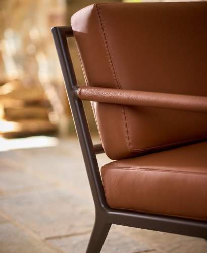 Close-up detail of a McKinnon and Harris deCamp armchair frame showcasing Foglizzo's soft cognac leather arm wrap and plush leather seat back cushion.