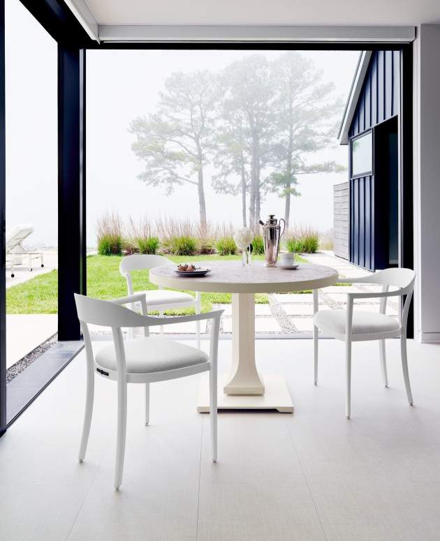 Chesapeake Dining Arm Chair finished in Classic White with upholstered seat pulled up to a Mundy Round Dining Table