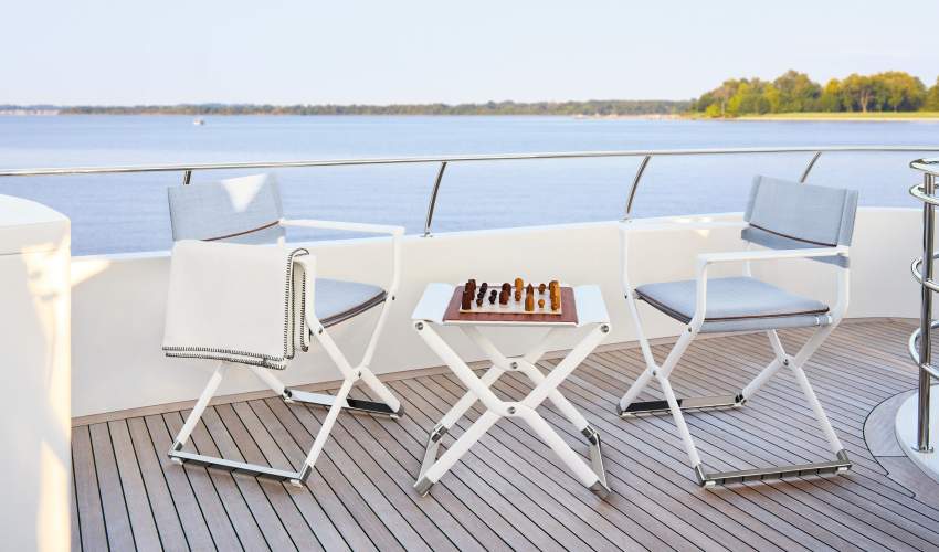 Upper deck of a yacht with white outdoor armchairs facing a wide view of open water and distant shoreline.